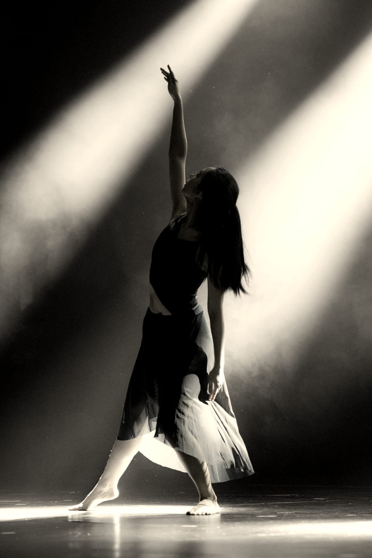 Dancer with one arm raised, caught in a shaft of light