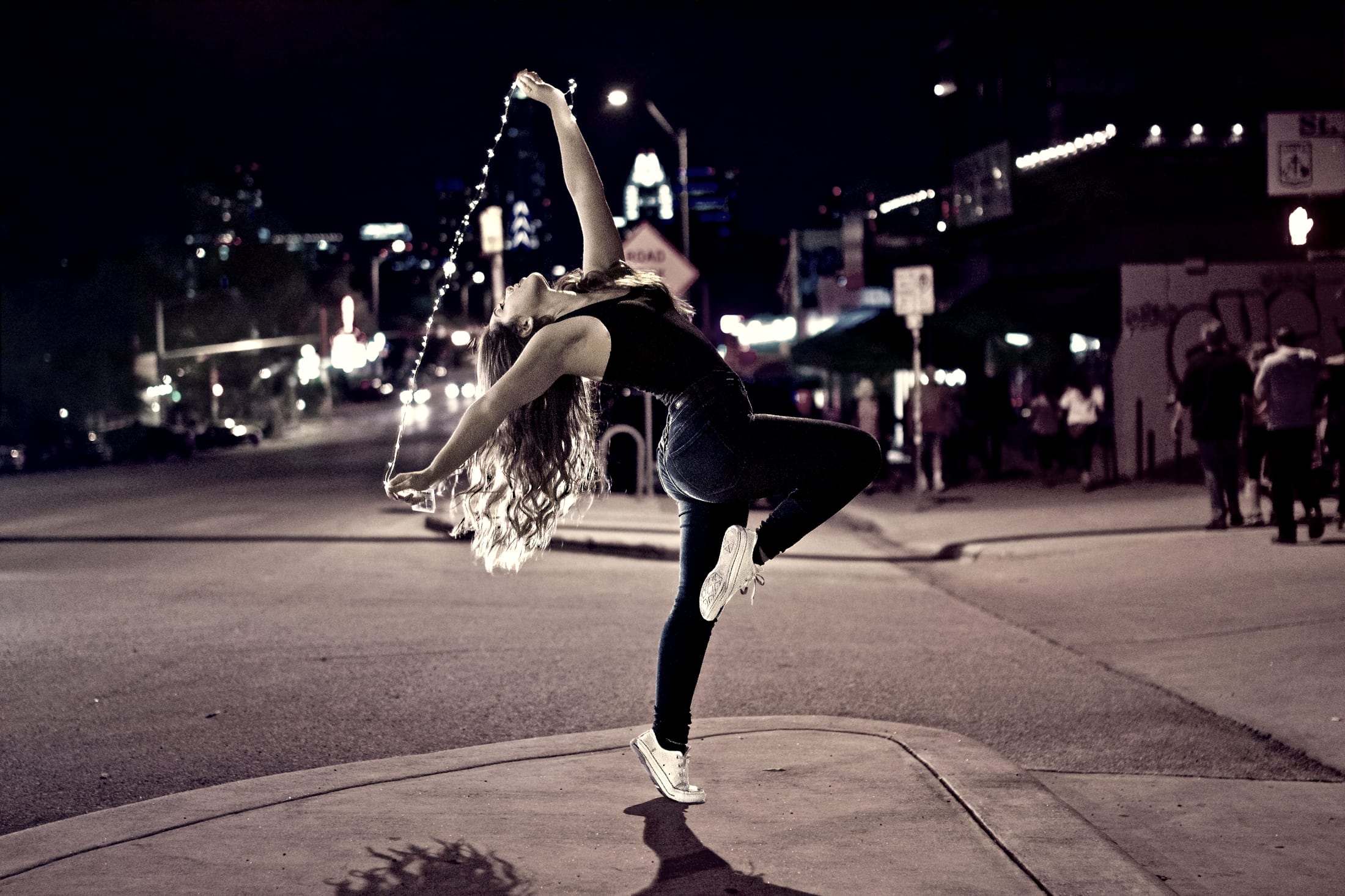 Dancer arching backwards on a city street at night, lights behind her